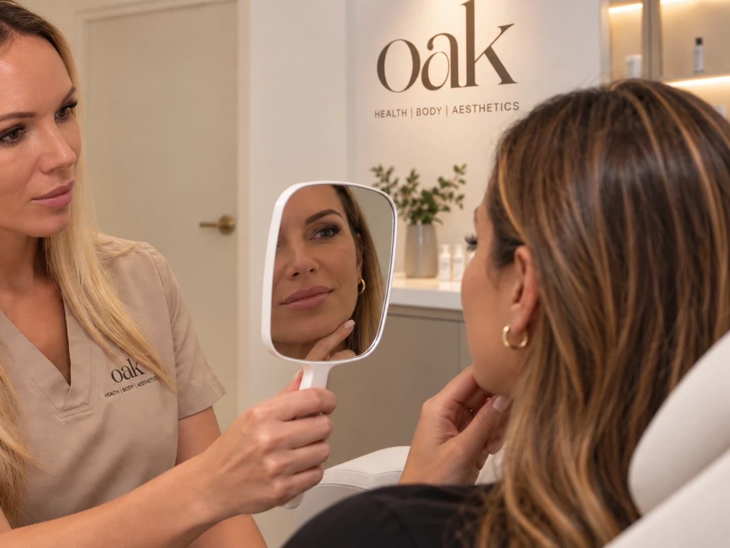 Kirby Shannon, Registered Nurse, holding a mirror for a client during a consultation at Oak